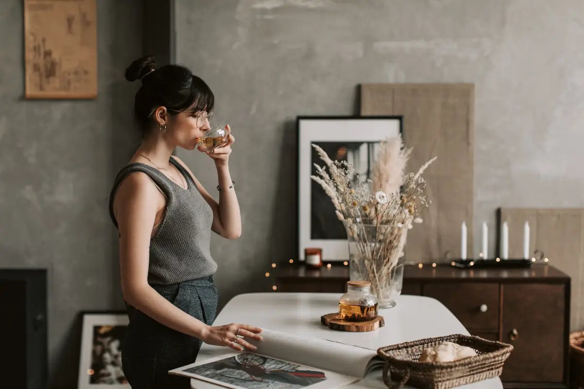 Woman enjoying a cup of tea in a cozy room with warm lighting and decor.